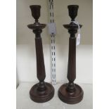 A pair of late 19thC turned and carved mahogany candlesticks with vase design sockets and tapered,