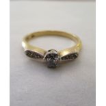 A gold coloured metal ring, set with a central diamond, flanked by chipped shoulders  stamped 18ct