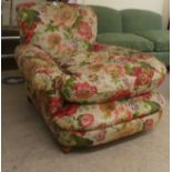 An early 20thC floral patterned fabric upholstered, low, enclosed armchair, raised on block feet