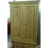 A modern pine two part wardrobe with a pair of panelled doors, enclosing a hanging rail, over a