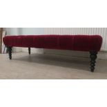 A modern long stool, part button upholstered in red fabric, over a stained wooden frame