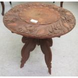 A mid 20thC fruitwood table, the top carved with a flower, raised on a folding base  19"h  18"dia