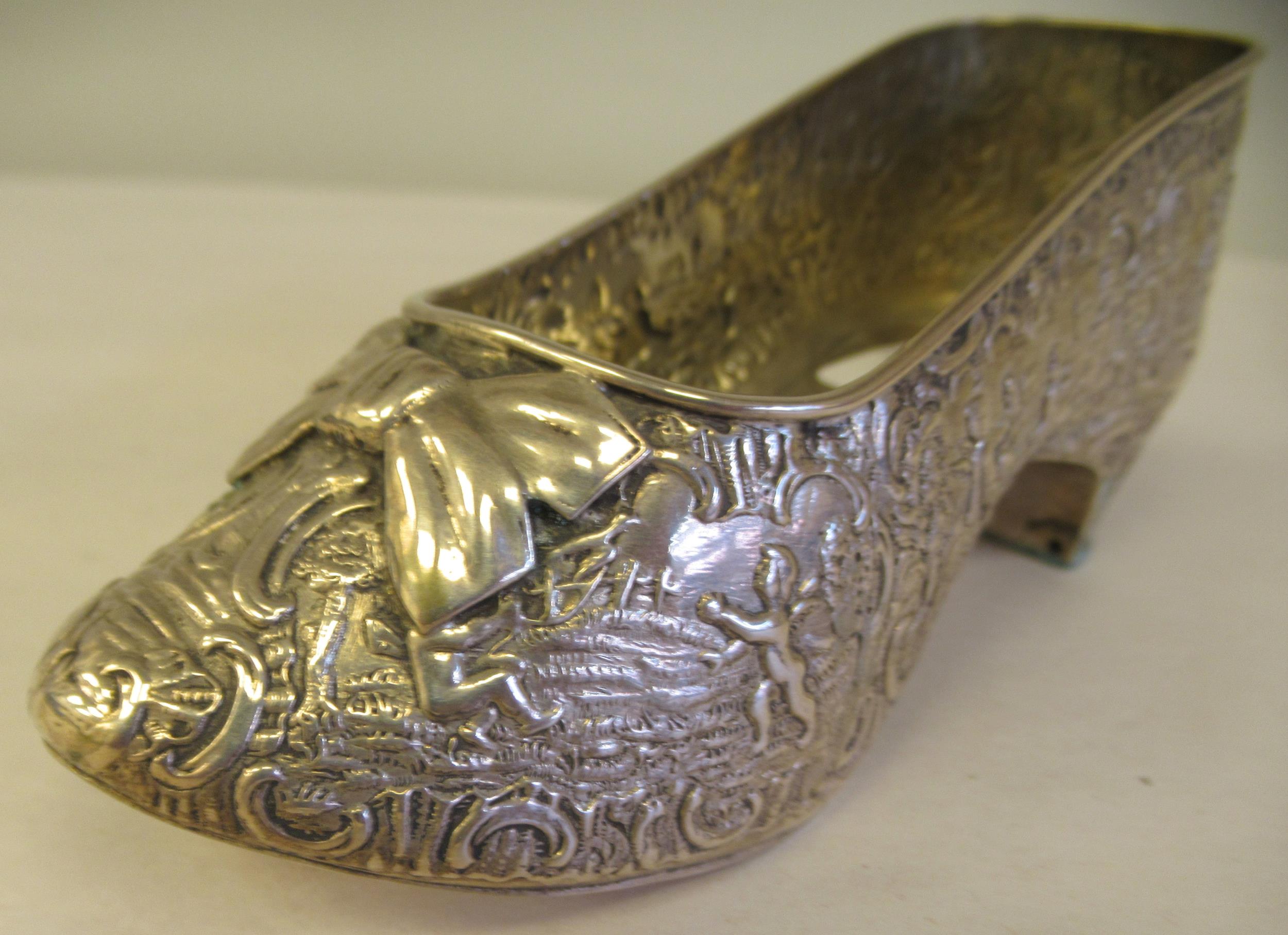 A Dutch silver coloured metal ornament, in the form of a lady's shoe, allover cast and chased with