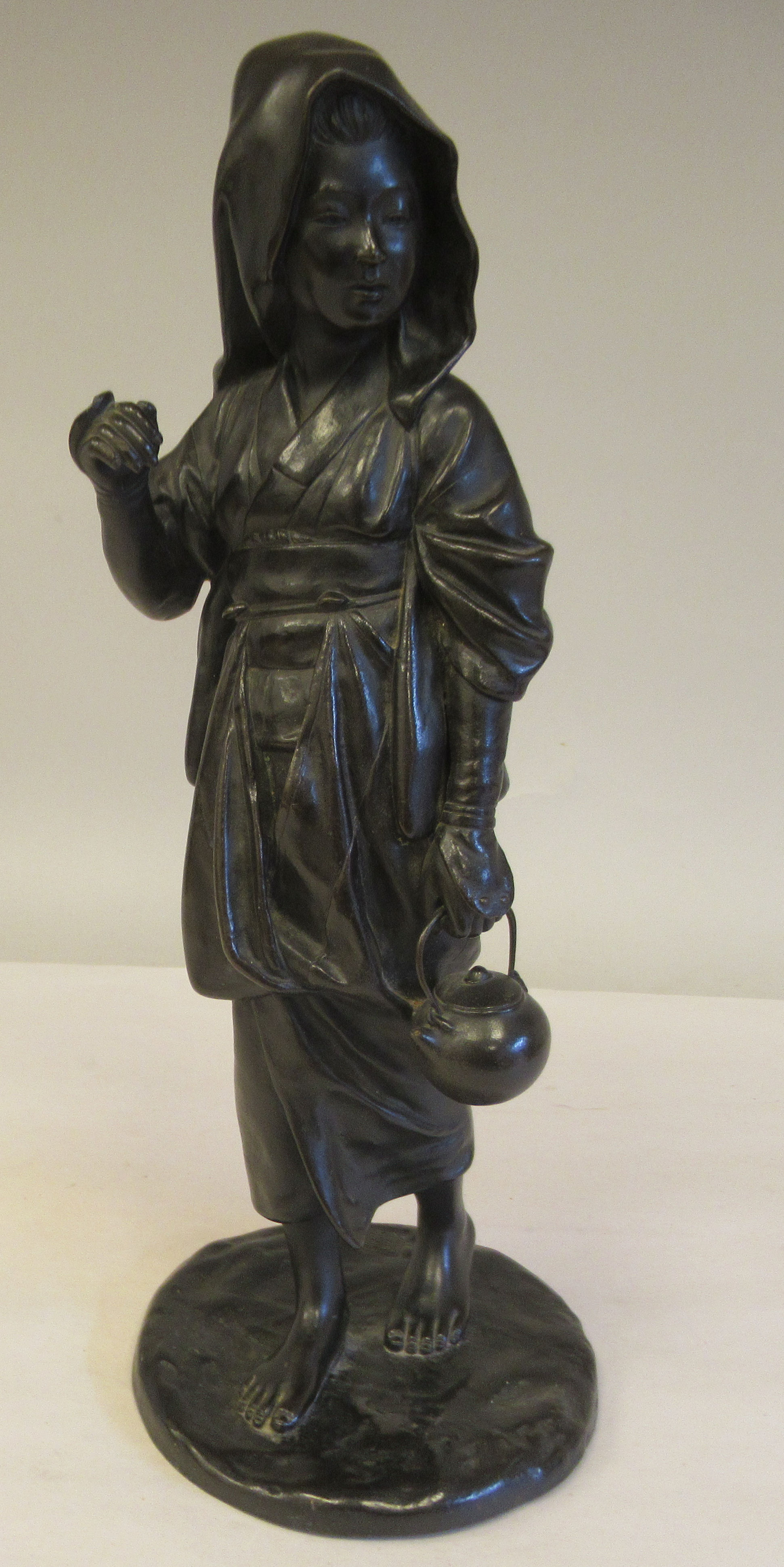 A late 19thC cast and patinated bronze figure, a young woman wearing traditional dress, walking with