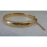 A 9ct gold hinged bangle, decorated with floral patterns