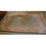 A Chinese washed woollen rug, decorated with vases of flowers and traditional designs, on a green