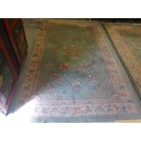 A Chinese washed woollen rug decorated with floral designs in pastel tones, on a green ground  76" x