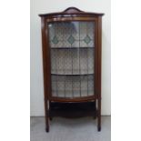 An Art Nouveau string inlaid mahogany bow front display cabinet with a lead glazed door, enclosing