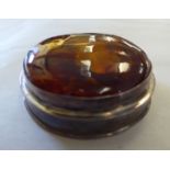 A round silver coloured metal shallow trinket box, the hinged lid set with an amber tablet