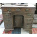 A George III mahogany kneehole desk with seven drawers around a recessed cupboard door, raised on