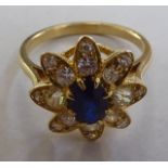 A yellow metal (probably 18ct) floral design ring, claw set with a central sapphire and surrounded