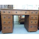An early 20thC oak nine drawer, twin pedestal desk with brass knob handles and a tooled, gilded hide