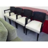 A set of four black stained oak framed elbow chairs with woven cane panelled backs and cream