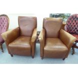 A pair of modern enclosed armchairs, upholstered in brown stitched hide, raised on stained beech
