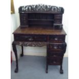 A late 19thC Chinese profusely carved padouk wood kneehole desk, the superstructure with a cupboard,