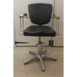 A modern black faux hide adjustable barbers chair, raised on a five spoke metal base