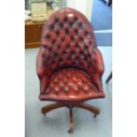 A modern bucket design office chair, stud and button upholstered in ox blood coloured hide, rotating