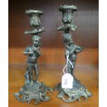 A pair of cast and lacquered brass candlesticks, each featuring a cherubic child, carrying a vase