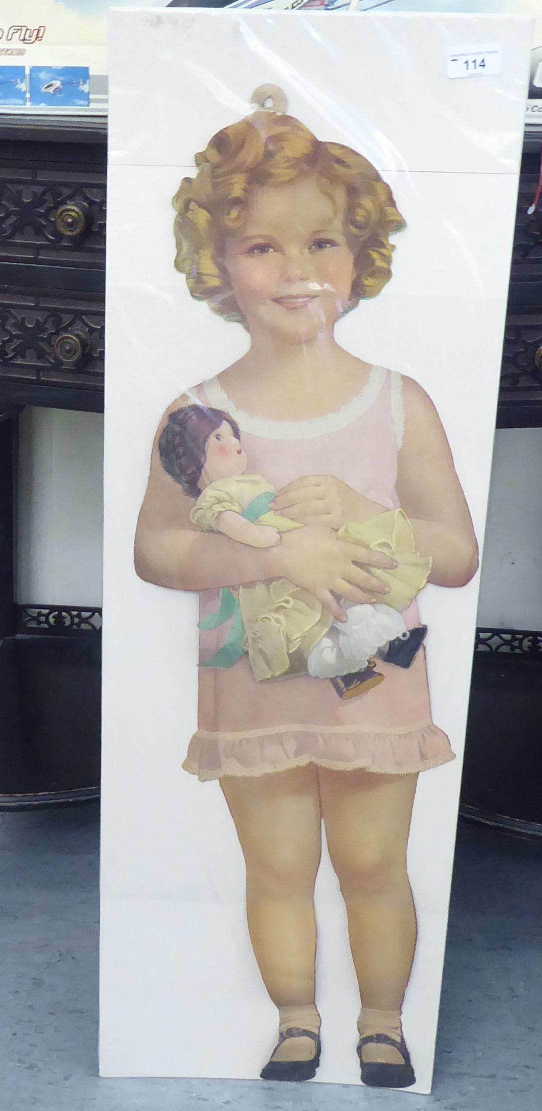 An early/mid 20thC printed cut-out card figure of a child with a baby doll  33"h on a wall hanger