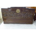 A mid 20thC Chinese camphorwood chest, the ornately carved decoration with a hinged lid, raised on