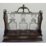 A mid 20thC French oak and silver plated tantalus, hosting three glass decanters with stoppers