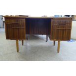 A circa 1970s mahogany and teak, one-piece, four drawer, twin pedestal desk, raised on turned,