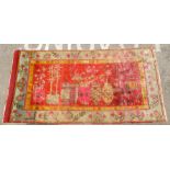 A Chinese carpet, decorated with a Khitan vase design, bordered by floral imagery, on a red and