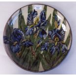 A painted and glazed terracotta charger, decorated with flowering irises, inscribed P&M Thomas,