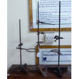 Three vintage chemists' laboratory flask stands with height adjustable stems, each set on a cast