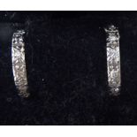A pair of white metal half-hoop earrings, each set with six diamonds