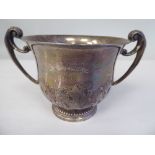 A silver porringer with a flared lip and opposing C-scrolled handles, on a demi-reeded footrim,