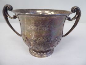 A silver porringer with a flared lip and opposing C-scrolled handles, on a demi-reeded footrim,