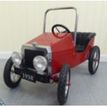 A painted model pedal car, in the manner of a veteran vehicle with red livery and spoked rubber