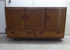 An Ercol honey coloured elm sideboard, comprising three inline doors, enclosing a fitted interior,