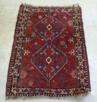 A Persian rug, decorated with two diamond shaped motifs, bordered by stylised designs, on a red