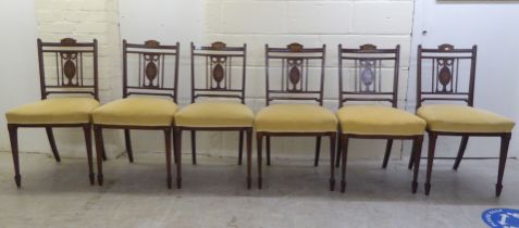 A set of six Edwardian mahogany framed splat back chairs, inlaid with musical ornament, raised on