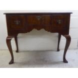 A George III crossbanded walnut and mahogany three drawer lowboy, raised on cabriole legs and pad