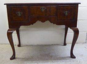 A George III crossbanded walnut and mahogany three drawer lowboy, raised on cabriole legs and pad