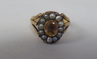 A yellow metal cluster ring, set with a central, oval cut imperial topaz, surrounded by pearls