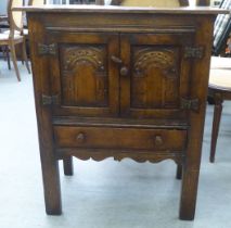 A 20thC Old English style oak side cabinet with a pair of carved panelled doors, over a single