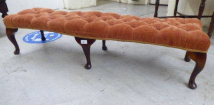 A modern footstool with an orange fabric, button upholstered top, raised on stained beech cabriole