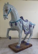 A Chinese style celadon coloured glazed ceramic model, a standing, bridled and saddled horse, on a