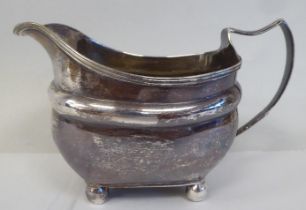 A George III silver oval, ogee shape cream jug with an applied wire rim and loop handle, on ball