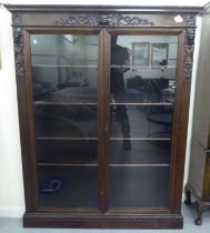 A late Victorian mahogany bookcase with carved mask ornament and two glazed doors, on a plinth  63"h