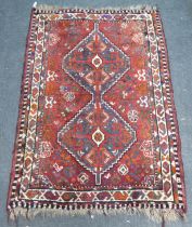 A Persian rug, decorated with two diamond shaped motifs, bordered by stylised designs, on a red