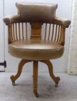 An early 20thC light oak framed desk chair with a round back and square, vertical rails, upholstered