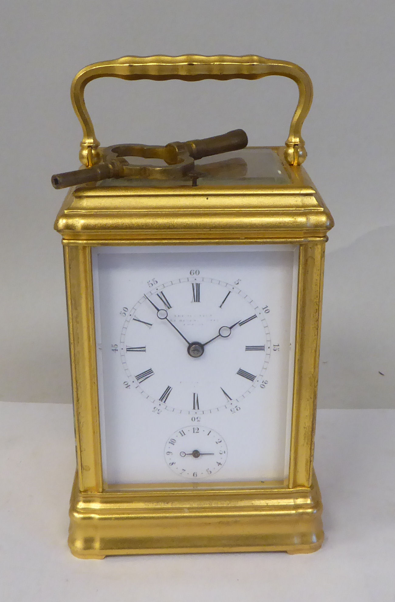 An early 20thC French lacquered brass cased carriage clock with a folding top handle and bevelled