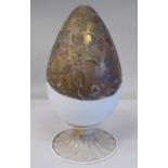 An antique Murano glass two part egg ornament, overpainted and gilded with floral designs, on a milk