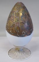 An antique Murano glass two part egg ornament, overpainted and gilded with floral designs, on a milk