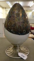 An antique Murano glass two part egg ornament, overpainted and gilded with floral designs, on a